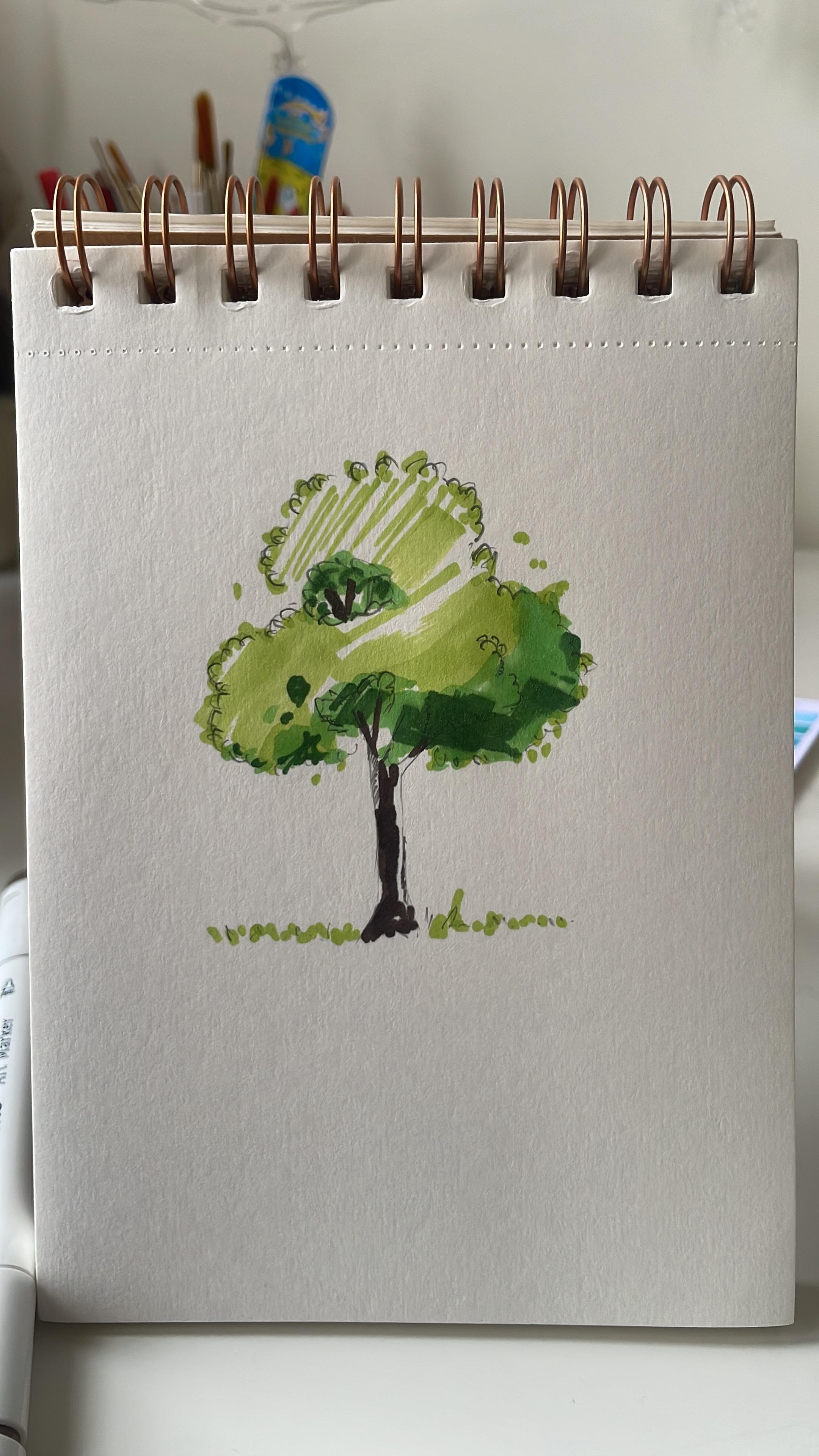 A compact green tree painted in watercolour and ink on a vertical spiral sketchbook page.